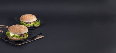 Öğle yemeği için siyah bir zemin üzerine iki hamburger. Fast food ve aperatifler. Metin için özgür yer. Uzay kopyalayın. Düz yatıyordu. Afiş