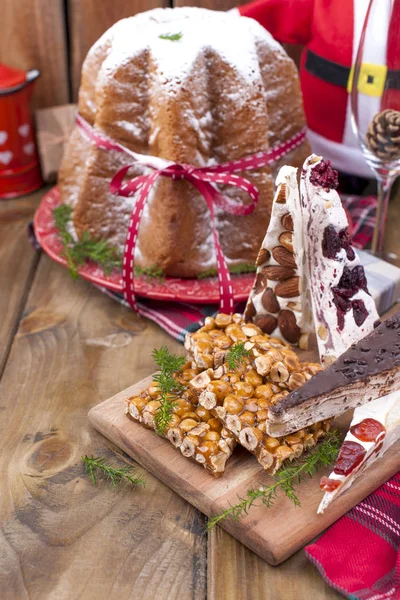 传统的意大利圣诞水果蛋糕 Panettone Pandoro 与节日红色丝带和糖果从坚果和牛轧糖 在一个木制的背景 文本的可用空间 — 图库照片