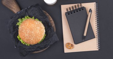 Büyük hamburger, bira ve bir siyah arka plan üzerinde planlama için defter. Fast food ve aperatifler. Metin için özgür yer. Düz yatıyordu. Kopya alanı