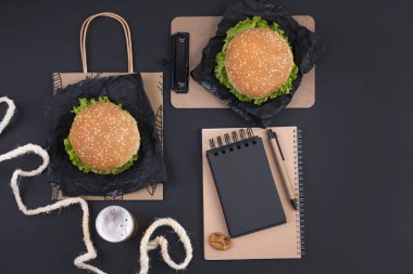 Büyük hamburger, bira ve bir siyah arka plan üzerinde planlama için defter. Fast food ve aperatifler. Metin için özgür yer. Düz yatıyordu. Kopya alanı