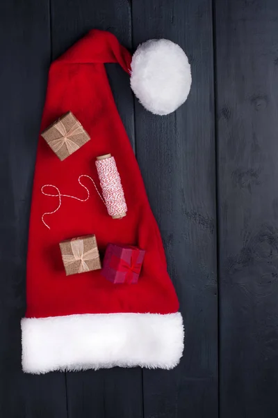 Rote Mütze Mit Bommel Weihnachtsmann Auf Schwarzem Holzgrund Geschenke Und — Stockfoto