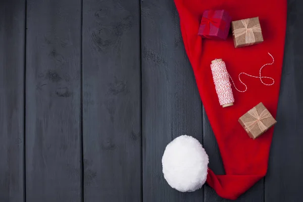 Rote Mütze Mit Bommel Weihnachtsmann Auf Schwarzem Holzgrund Geschenke Und — Stockfoto