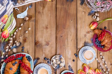 Paskalya kahvaltısı taze kahve, böğürtlen ve hamur işleri, turuncu laleler, pastırmalı kruvasanlar ve çeşitli tatlılar, renkli bıldırcın yumurtaları ve bahar tatili süslemeleriyle yatıyordu. Üst Manzara. Boşluğu kopyala