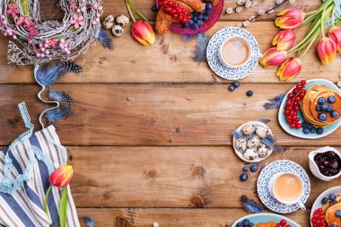 Paskalya kahvaltısı taze kahve, böğürtlen ve hamur işleri, turuncu laleler, pastırmalı kruvasanlar ve çeşitli tatlılar, renkli bıldırcın yumurtaları ve bahar tatili süslemeleriyle yatıyordu. Üst Manzara. Boşluğu kopyala