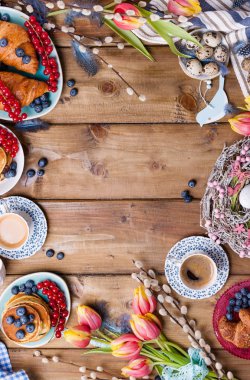 Paskalya kahvaltısı taze kahve, böğürtlen ve hamur işleri, turuncu laleler, pastırmalı kruvasanlar ve çeşitli tatlılar, renkli bıldırcın yumurtaları ve bahar tatili süslemeleriyle yatıyordu. Üst Manzara. Boşluğu kopyala