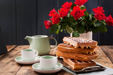 Kahvaltıda iki kişilik Belçika waffle 'ı. Ev yapımı hamur işleri ve masada bir buket kırmızı gül. Lezzetli romantik öğle yemeği. Metin için boş alan