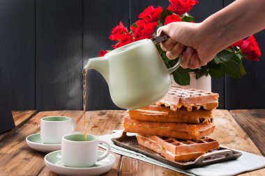 Kahvaltıda iki kişilik Belçika waffle 'ı. Ev yapımı hamur işleri ve masada bir buket kırmızı gül. Lezzetli romantik öğle yemeği. Sevgililer Günü için fotoğraf ve kadınlar gününde sürpriz.