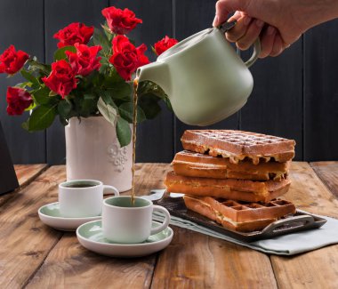 Kahvaltıda iki kişilik Belçika waffle 'ı. Ev yapımı hamur işleri ve masada bir buket kırmızı gül. Lezzetli romantik öğle yemeği. Metin için boş alan