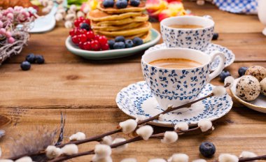 Antika bir fincanda taze aromatik kahve, kahvaltıda yaban mersini ve üzümlü ev yapımı hamur işleri, ahşap arka planda ve bahar lalelerinde. Metin için boş alan