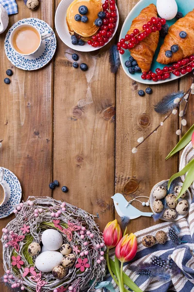 Paskalya kahvaltısı taze kahve, böğürtlen ve hamur işleri, turuncu laleler, pastırmalı kruvasanlar ve çeşitli tatlılar, renkli bıldırcın yumurtaları ve bahar tatili süslemeleriyle yatıyordu. Üst Manzara. Boşluğu kopyala