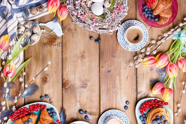 Paskalya kahvaltısı taze kahve, böğürtlen ve hamur işleri, turuncu laleler, pastırmalı kruvasanlar ve çeşitli tatlılar, renkli bıldırcın yumurtaları ve bahar tatili süslemeleriyle yatıyordu. Üst Manzara. Boşluğu kopyala