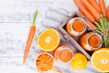 Havuçtan taze meyve suyu, portakal ve limon. Ahşap zemin üzerinde yapraklı havuç ve diğer taze meyveler. Kutuda iç, üstten bak.