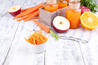 Taze havuç, elma, portakal ve limon suyu. Beyaz ahşap arka planda yapraklı havuç ve diğer taze meyveler. Kutuda iç ve doğranmış havuç.