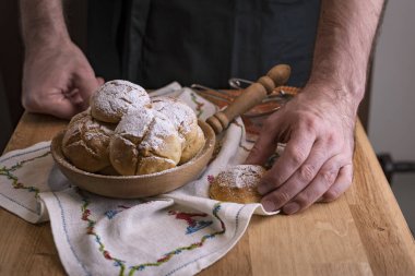 Siyah önlüklü bir adam ev yapımı pastaları tatlı bir şekilde hazırlar. Erkeklerin elindeki tahta masada şekerli çörekler. Metin için boş alan