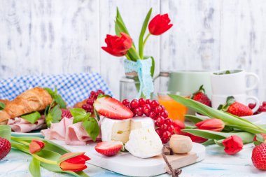 Ayçöreği ve pastırmalı tatlı bahar kahvaltısı. Bir buket kırmızı lale ve taze çilek ve kuşüzümü. Tatil kutlaması konsepti. Kahvaltı için peynir.