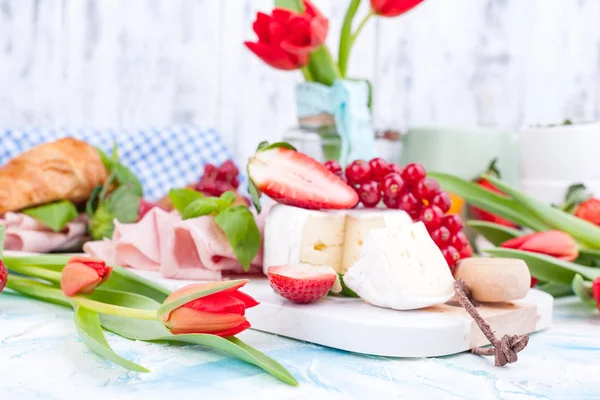 Ayçöreği ve pastırmalı tatlı bahar kahvaltısı. Bir buket kırmızı lale ve taze çilek ve kuşüzümü. Tatil kutlaması konsepti. Kahvaltı için peynir.
