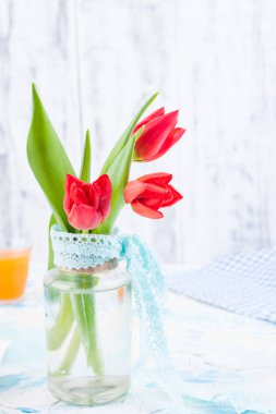 Beyaz bir masadaki vazoda duran bir buket taze kırmızı lale. Çiçekli Paskalya kahvaltısı ve metin için boş yer.