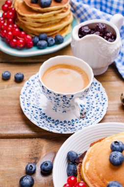 Kahvaltıda yaban mersinli krep ve üzümlü frenk üzümü ve taze aromatik kahve. Tahta bir masada çiçekli bahar kahvaltısı. Tatil ve Paskalya konsepti