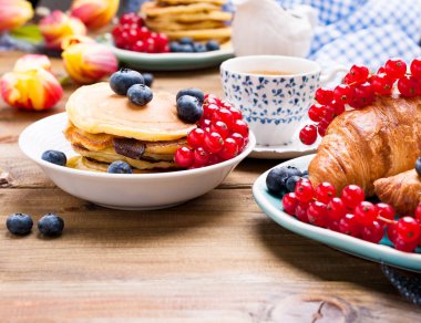 Kahvaltıda yaban mersinli krep ve üzümlü frenk üzümü ve taze aromatik kahve. Tahta bir masada çiçekli bahar kahvaltısı. Tatil ve Paskalya konsepti