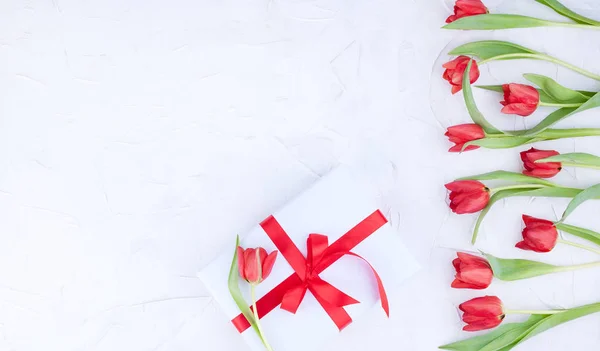 A bouquet of red tulips and a box with a bow on a white backgrou