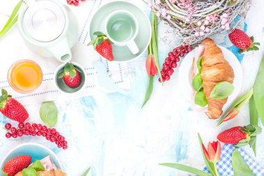 Bayram için çeşitli lezzetlerle kahvaltı ya da yemek masası. Yumuşak peynirli taze çilek ve üzümler ve kırmızı bahar laleleri. Kahve fincanları masada, kruvasanlar ve kırmızı laleler.