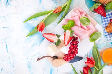 Kahvaltıda ya da öğle yemeğinde küflü, taze çilekli yumuşak beyaz peynir. Paskalya bayramı için kırmızı bahar laleleri. Üst görünüm