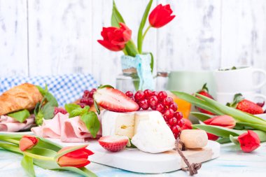 Kahvaltı ya da Paskalya yemekleri için çeşitli lezzetler içeren bir akşam yemeği masası. Yumuşak peynirli taze çilek ve üzümler ve kırmızı bahar laleleri. Tatil için içecekler ve atıştırmalıklar. Boşluğu kopyala