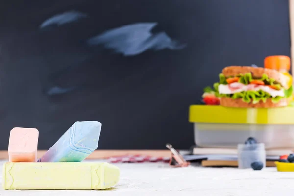 Schachtel mit Schulessen neben der Tafel. Gesunde Ernährung für ein Kind. Toast mit Salat und Erdbeeren und Blaubeeren und einer Flasche Saft. Essen und Bücher für das Institut oder die Schule. Kopierraum. — Stockfoto