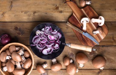 Ahşap arka planda kırmızı soğan ve baharatlı Champignon mantarları, ahşap çatal bıçaklar. Kırsal bir fotoğraf. Sebzeli vejetaryen yemeği. Metin için yer
