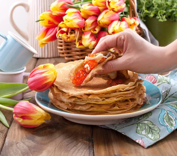Pancake dengan kaviar dan mentega di tangan seorang wanita, karangan bunga — Stok Foto