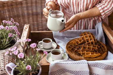 Kadınlar elinde bir su ısıtıcısı tutar ve kupaya çay döker. Ev yapımı breakfas