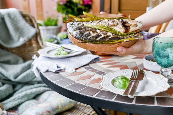 Dişi ellerde bir tabakta kızarmış balık. Differen ile yemek masası