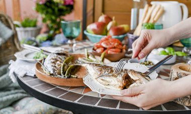 Dişi ellerde bir tabakta kızarmış balık. Differen ile yemek masası