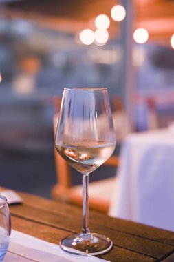 Restoranda masada bir kadeh beyaz şarap. Tonlu fotoğraf. Parlama ve ışık lekeleri. Metin için boş alan.