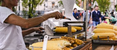 Izgara mısır. Şehir merkezinde turistler için fast food. Sokaklarda yemek satmak. Alıcı ve satıcı çerçevesinde eller.
