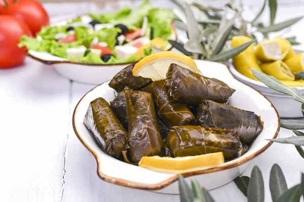 Traditional greek cuisine. Wrapped rice in grape leaves. Dolma with lemon, spices and greek salad. Home cooked food. Olive branches and various spicy appetizers.