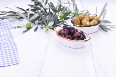 Geleneksel mezeler, Yunan mutfağından yeşil ve kırmızı zeytinler. Beyaz ahşap arka plan. Taze zeytin dalları. Boşluğu kopyala.
