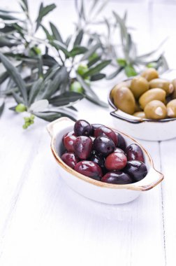 Geleneksel mezeler, Yunan mutfağından yeşil ve kırmızı zeytinler. Beyaz ahşap arka plan. Taze zeytin dalları. Boşluğu kopyala.