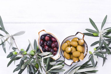 Geleneksel mezeler, Yunan mutfağından yeşil ve kırmızı zeytinler. Beyaz ahşap arka plan. Taze zeytin dalları. Uzayı kopyala Yukarıda.