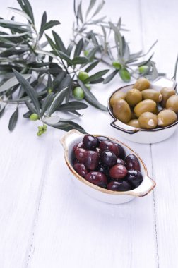 Geleneksel mezeler, Yunan mutfağından yeşil ve kırmızı zeytinler. Beyaz ahşap arka plan. Taze zeytin dalları. Boşluğu kopyala.