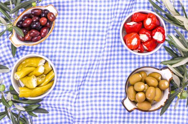 Geleneksel mezeler, Yunan mutfağından yeşil ve kırmızı zeytinler. Taze zeytin dalları. Uzayı kopyala Yukarıdan. Mavi kareli masa örtüsü.