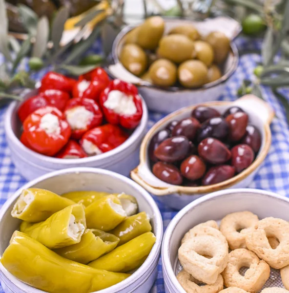 Geleneksel mezeler, Yunan mutfağından yeşil ve kırmızı zeytinler. Taze zeytin dalları. Uzayı kopyala Mavi kareli masa örtüsü.