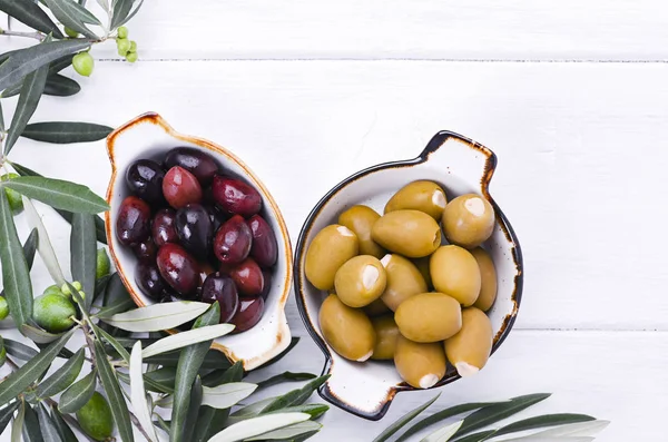 Traditional appetizers, green and red olives from Greek cuisine. White wood background. Fresh branches of olives. Copy space. Above