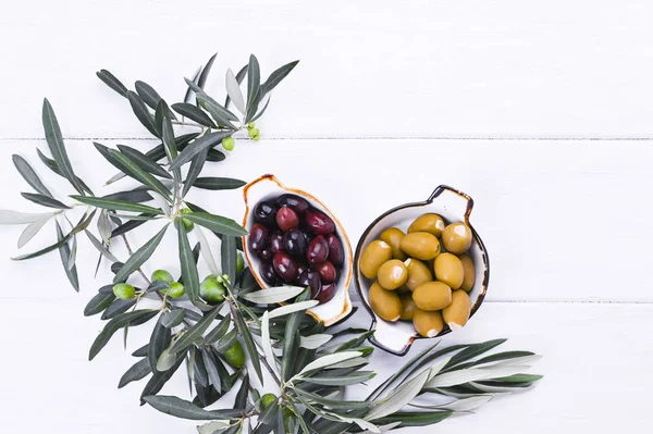 Traditional appetizers, green and red olives from Greek cuisine. White wood background. Fresh branches of olives. Copy space. Above