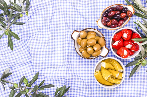 Geleneksel mezeler, Yunan mutfağından yeşil ve kırmızı zeytinler. Taze zeytin dalları. Uzayı kopyala Yukarıdan. Mavi kareli masa örtüsü.