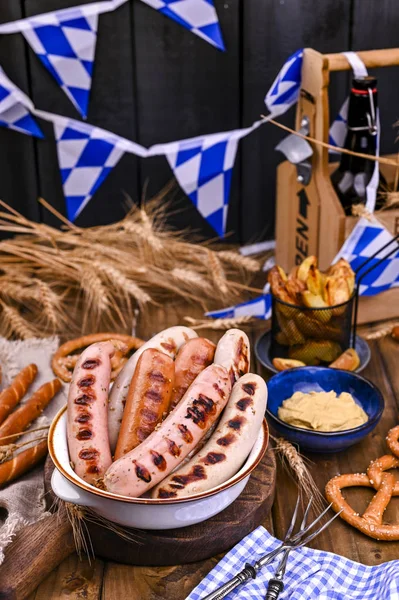 German sausages on the grill. Traditional German sausages and pastry brezel for a beer festival. Wood background and decor.