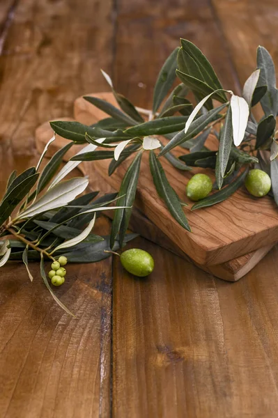 green olives, olives oil and wooden serving board over light wooden background. Top view, free space for text