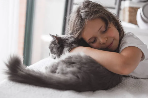 A menina abraça um gato em uma cama em um quarto. A amizade de pessoas e animais. Relações e amor para animais de estimação — Fotografia de Stock