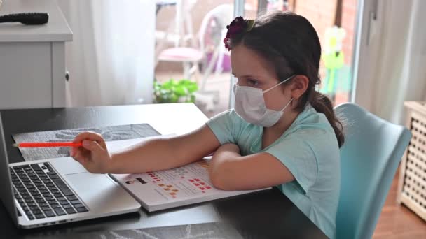 遠隔オンライン教育。デジタルタブレットノートパソコンを持つ女子高生と学校の宿題をする、医療マスクの子供は学校から宿題をします。焦点を合わせて。コピースペース。隔離 — ストック動画