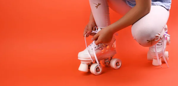 Kleines Kind mit Rollschuhen, blauem Helm auf rotem Grund, Schnürsenkel binden. Ein Mädchen von 7 Jahren posiert und bereitet sich auf die aktive Freizeit auf Retro-Schlittschuhen vor. Kopierraum. — Stockfoto